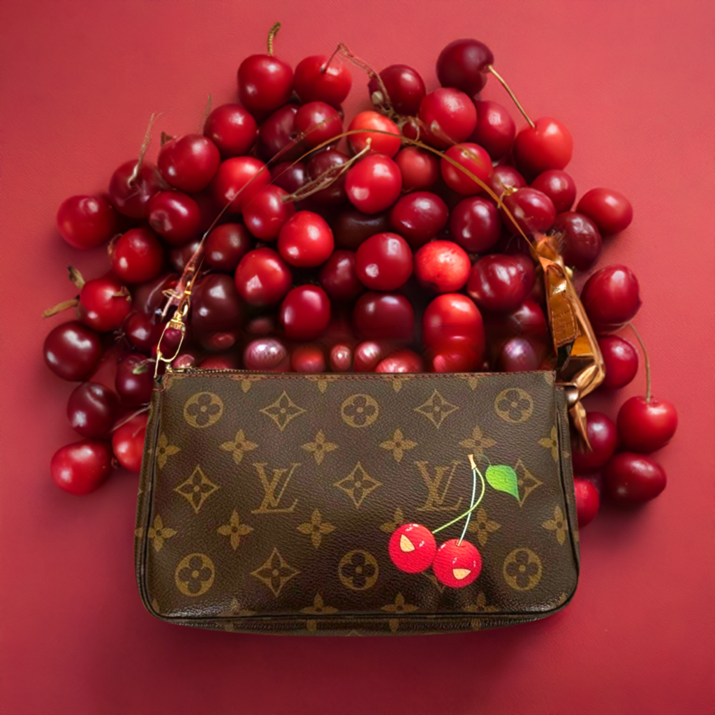 Picture of a Louis Vuitton cherry pochette lying on a pile of cherries on a red background