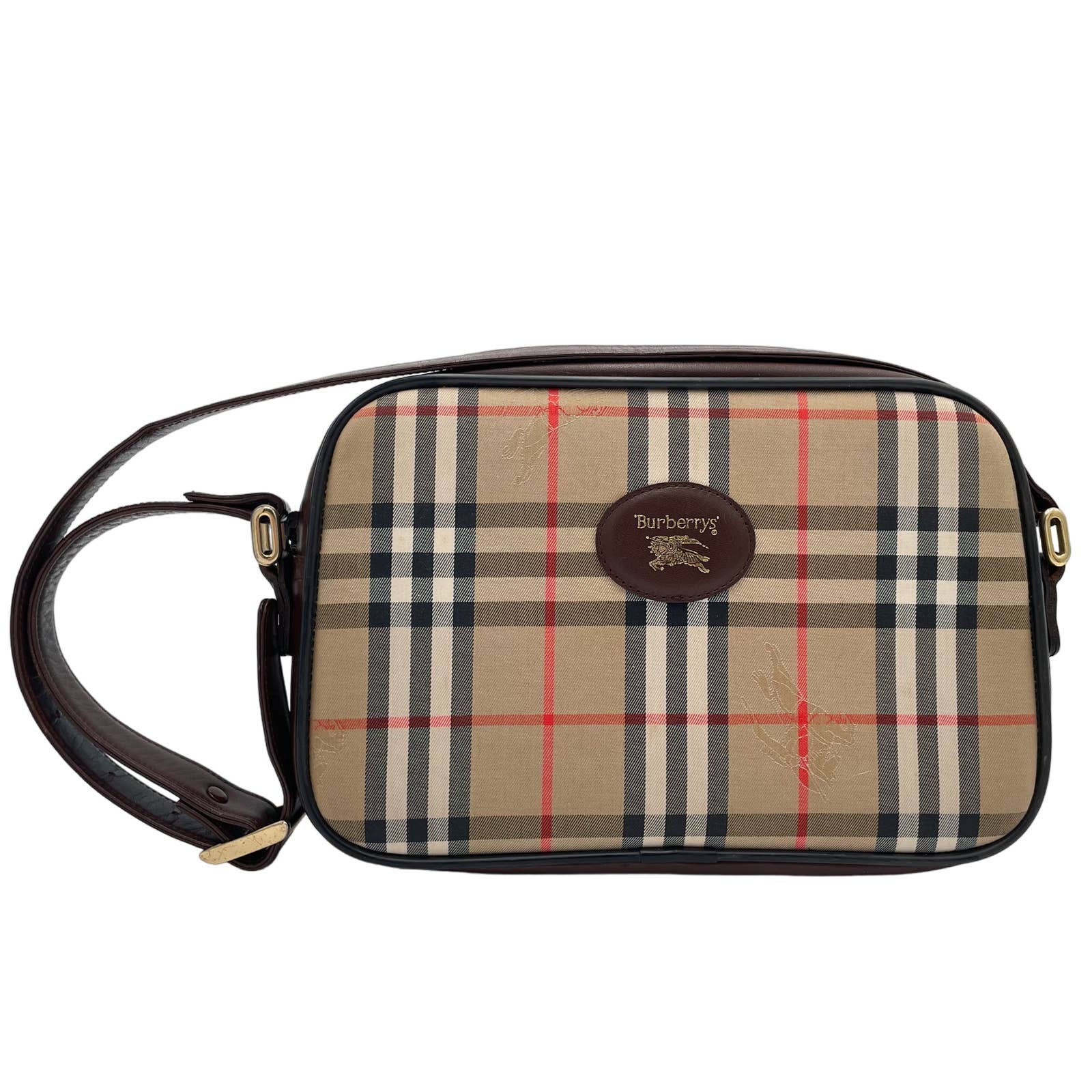 A rectangular Burberry Crossbody Bag featuring the signature beige, black, red, and white pattern. The bag has a dark brown adjustable leather strap and a brown leather patch with the brand's logo embossed on the front.