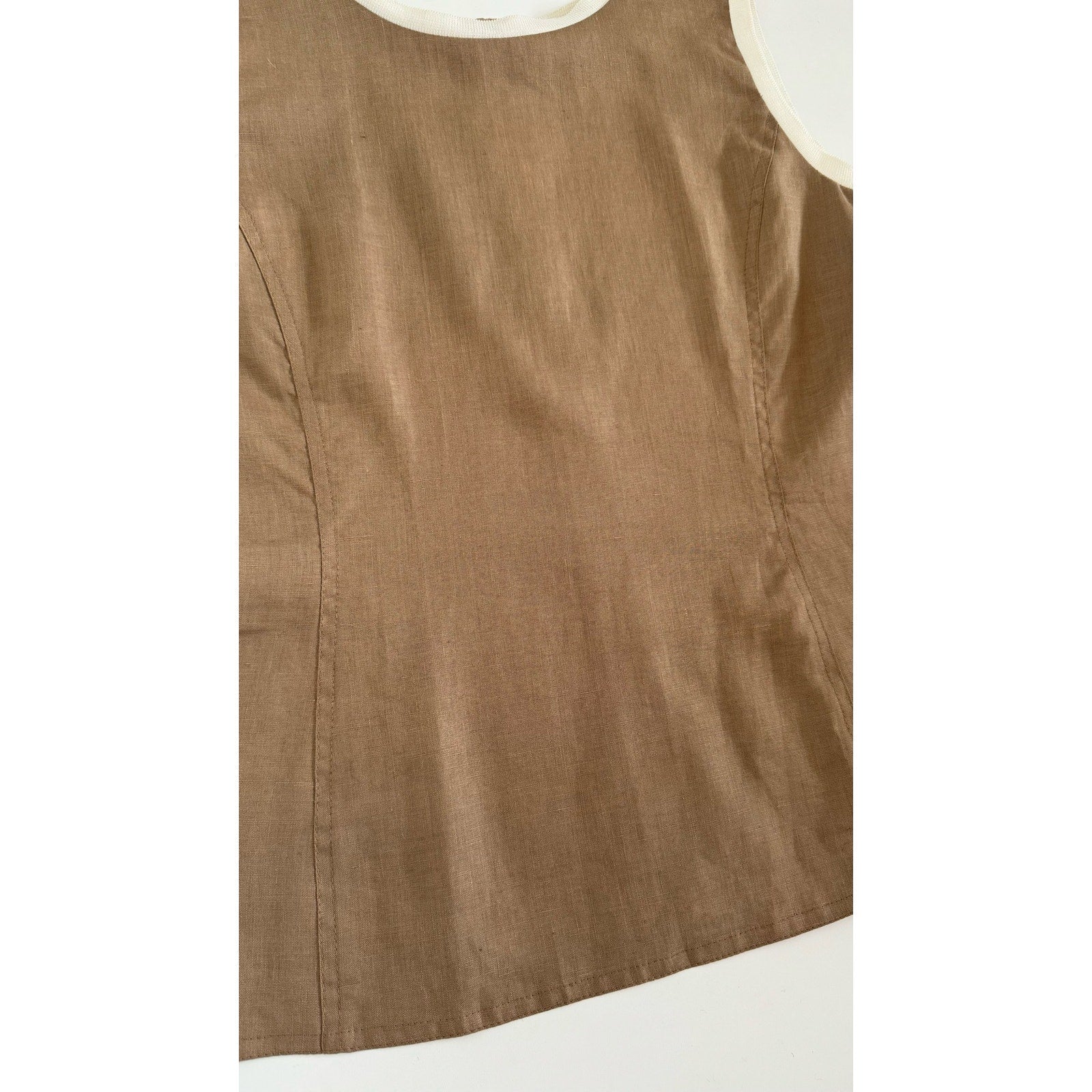 A sleeveless brown blouse with white trim around the collar and armholes. Made from 100% linen, the fabric appears to be lightweight and slightly textured. Perfect as a summer top, the Valentino Miss V Linen Tank Top has a simple, elegant design reminiscent of vintage Valentino Miss V.