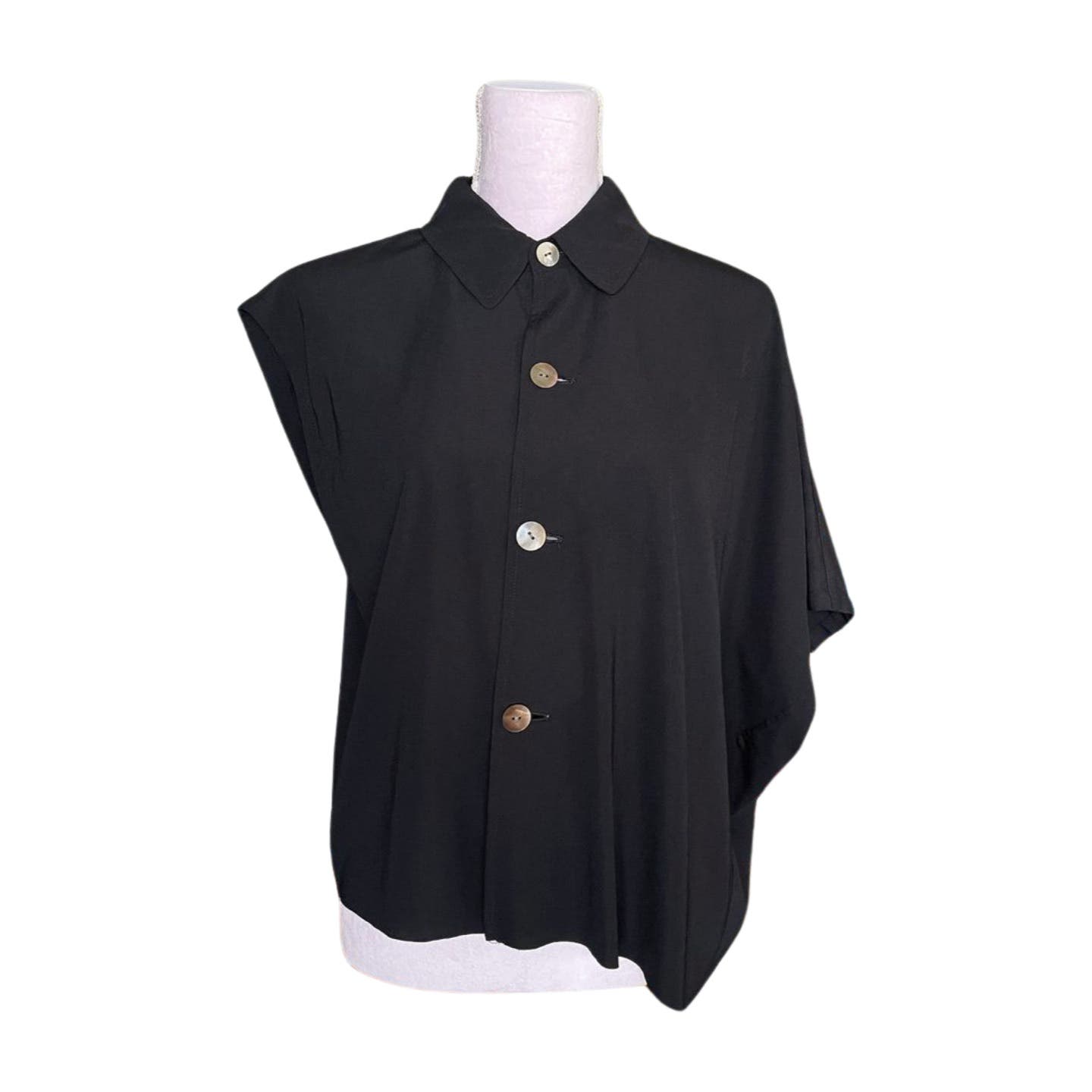 A black asymmetrical short-sleeve tricot blouse on a mannequin with buttons down the front. Made of luxurious polyester, the Vintage 1992 Comme des Garcons Asymmetric Top by Comme des Garçons features a collar and three buttons ranging from light to dark. The left shoulder appears lower and more draped than the right, reminiscent of Comme des Garçons' avant-garde style.