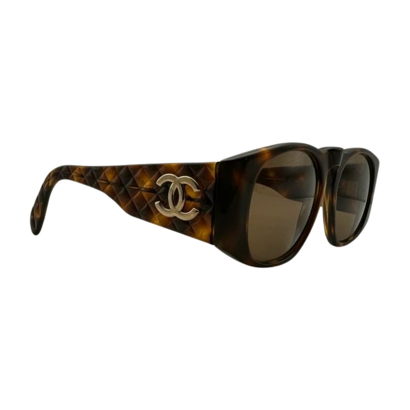 A pair of Vintage 90’s Chanel Sunglasses featuring dark lenses and quilted arms. The tortoiseshell sides are adorned with a gold interlocking double "C" logo, adding a touch of luxury to the design.