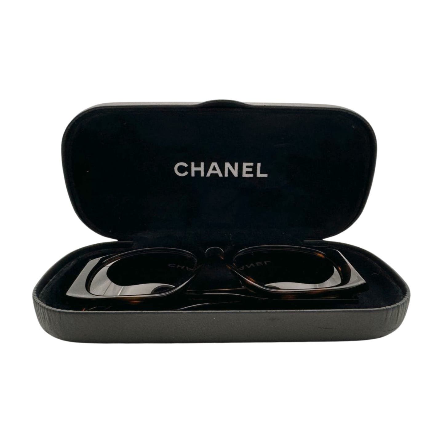 A pair of dark brown Chanel Vintage 90’s Sunglasses in a black Chanel-branded hard case, displayed open. The case interior features a soft, black lining with the "CHANEL" logo prominently printed on the upper lid. The glasses have thick, rectangular frames and tortoise shell quilted arms for added elegance.