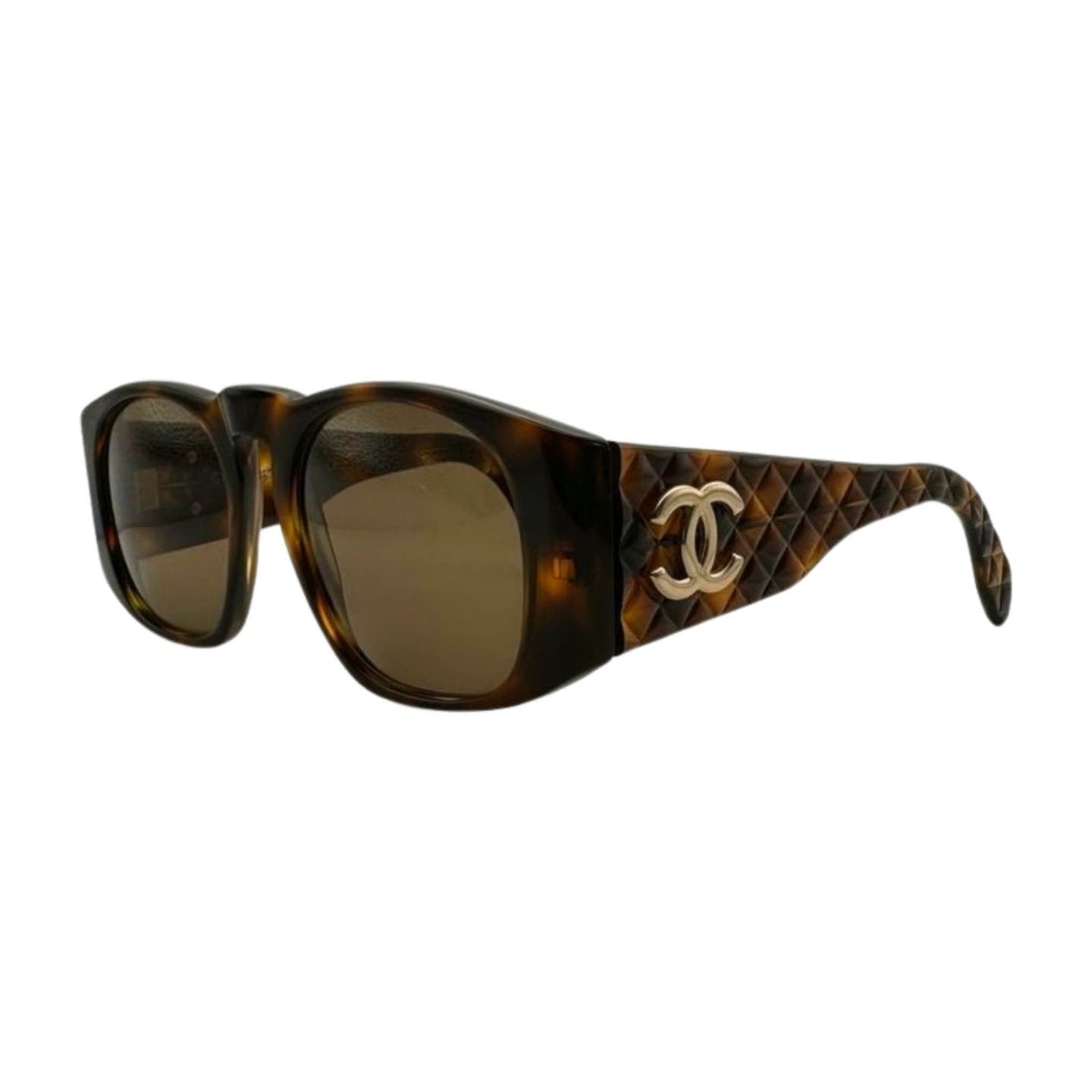 A pair of Vintage 90’s Chanel Sunglasses with a tortoise shell frame and dark lenses. The quilted arms feature a prominent, interlocking CC logo in silver on the sides. The design is elegant and iconic.