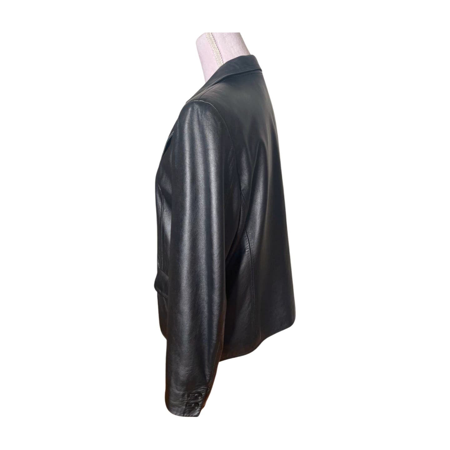 A Vintage Balmain Black Leather Blazer displayed on a mannequin is shown from the side. The blazer features a classic design with long sleeves, a smooth, shiny texture, and a polyester lining. The mannequin's pink neck covering is slightly visible, providing contrast to the black leather. Professional cleaning is recommended.