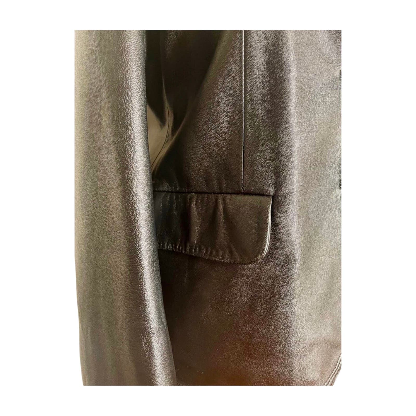 Close-up of a Vintage Balmain Black Leather Blazer with a polyester lining. The image focuses on the texture of the leather and a single pocket with a flap on the right side. The blazer appears high-quality with fine stitching details, suggesting it would benefit from professional cleaning to maintain its pristine condition.