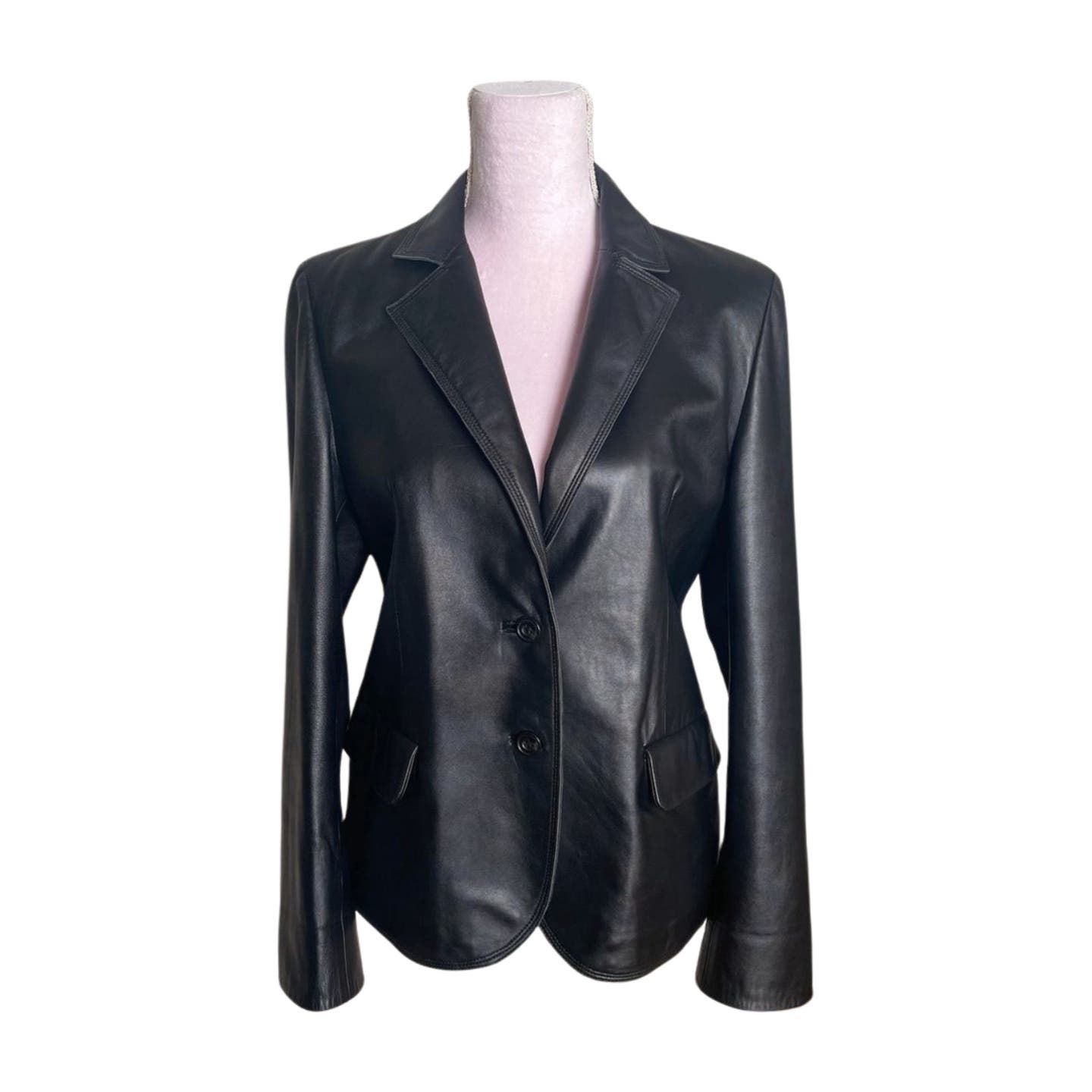 A sleek Vintage Balmain Black Leather Blazer is displayed on a mannequin. The blazer, complete with polyester lining, features a notched collar, two front buttons, and flap pockets on either side. The design is tailored with long sleeves and a smooth, polished finish. Recommended for professional cleaning only.