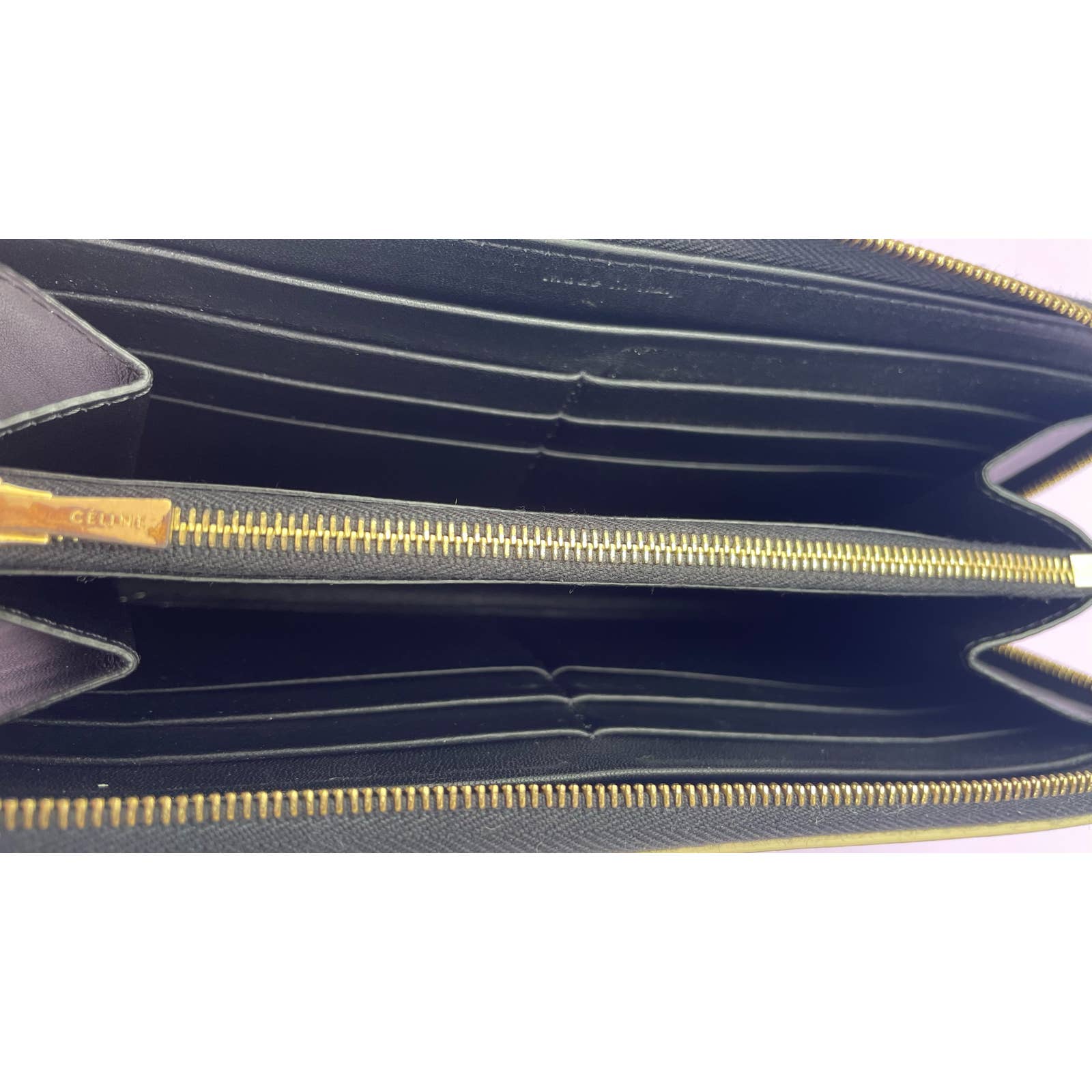 The image shows the inside of a Celine Celine Alphabet Wallet Gold with a gold zipper. The black patent leather wallet has several card slots on both sides and a central compartment for storing items like cash or coins. The zipper closure and the wallet's edges have a clean and neatly finished look.