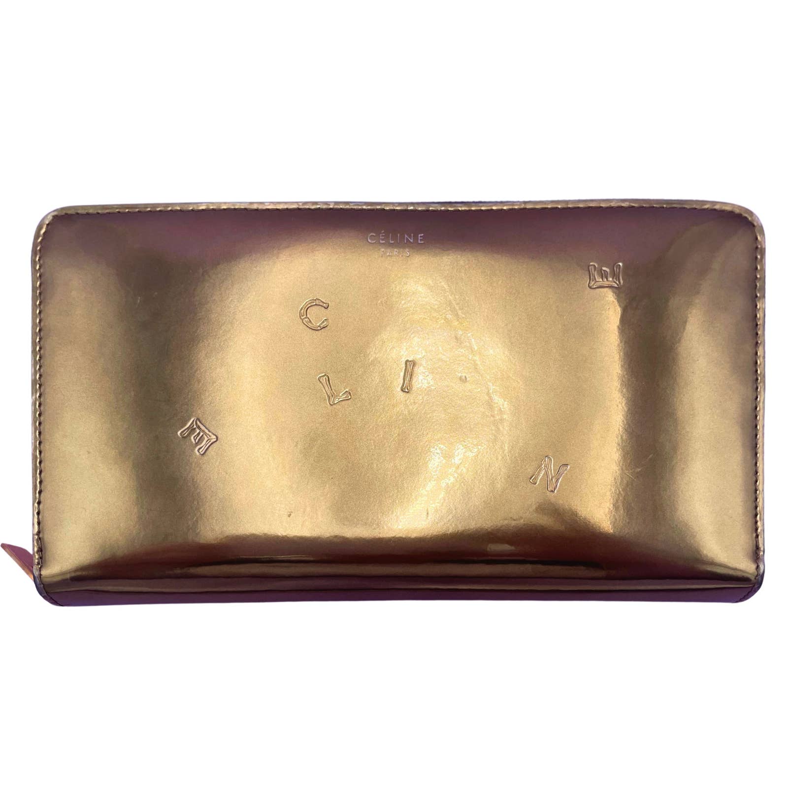 The Celine Alphabet Wallet Gold is a rectangular, metallic gold-colored accessory crafted from patent leather. "CELINE" is embossed at the center, with the letters scattered randomly across its shiny surface. It features a zipper closure to keep your essentials secure.